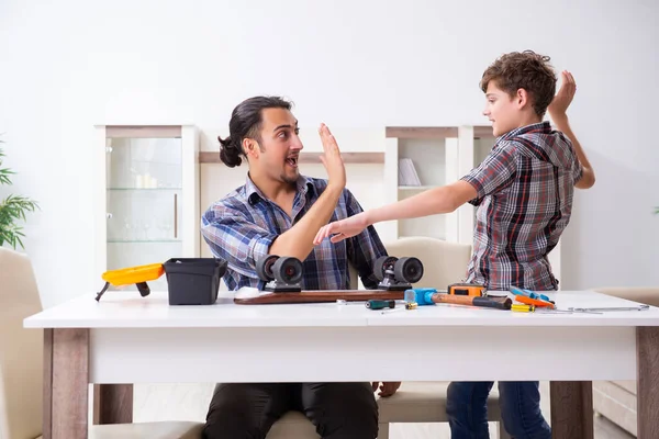 Young father repairing skateboard with his son at home — Stock Photo, Image