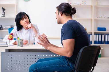 Genç erkek hasta yaşlı kadın doktoru ziyaret ediyor.