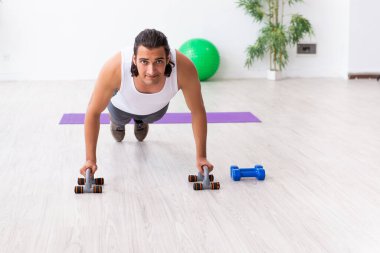 Genç yakışıklı adam içeride spor yapıyor.