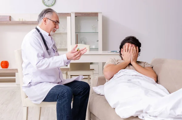 Old male doctor visiting young male patient — Stock Photo, Image