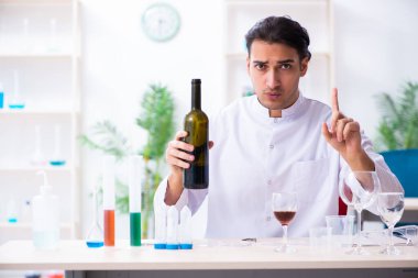 Erkek kimyager laboratuvarda şarap örneklerini inceliyor.