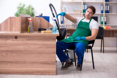 Genç yakışıklı müteahhit ofisi temizliyor.