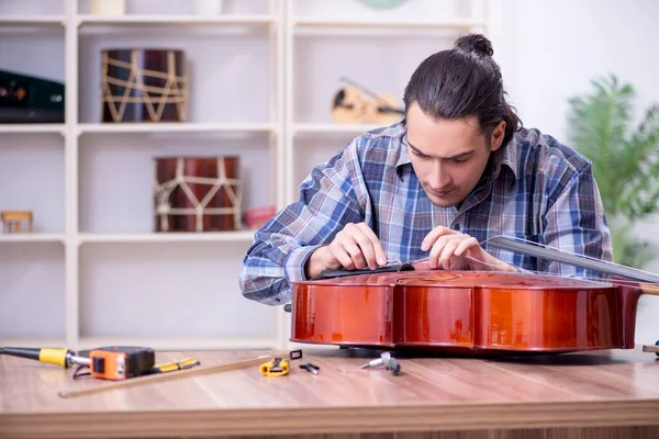 Mladý pohledný opravář opravuje violoncello — Stock fotografie