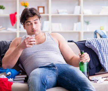 Dağınık bir odada alkol alan genç bir öğrenci.