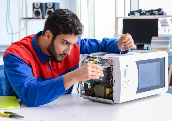 Genç tamirci mikrodalga fırını tamir ediyor ve onarıyor. — Stok fotoğraf