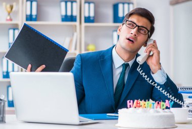 Genç işadamı ofiste tek başına doğum gününü kutluyor.