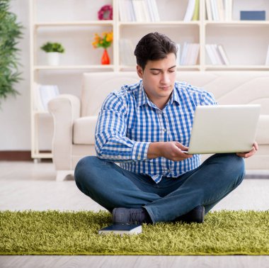 Genç yakışıklı adam evde yerde oturuyor.