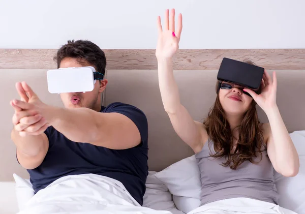 Wife and husband with virtual reality goggles in the bed