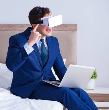 Yatak odasında sanal gerçeklik kulaklığı takan bir iş adamı.