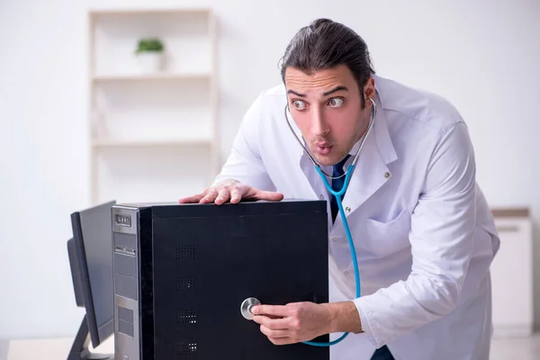 Young male doctor with stethoscope repairing computer — Stock Photo, Image