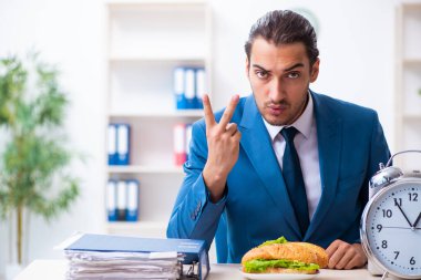 Genç erkek çalışan işyerinde kahvaltı yapıyor.