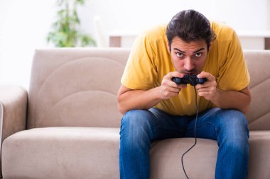 Genç adam evde joystick oynuyor.
