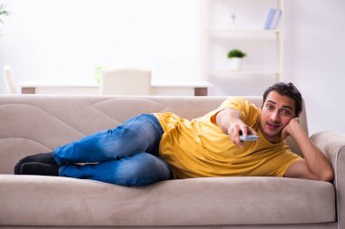 Genç adam evde televizyon izliyor.