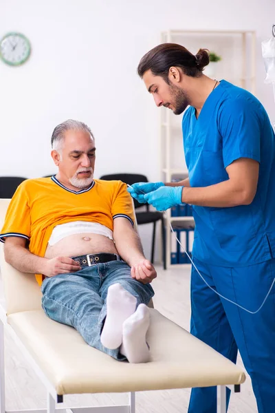 Yaşlı adam genç erkek doktoru ziyaret ediyor.