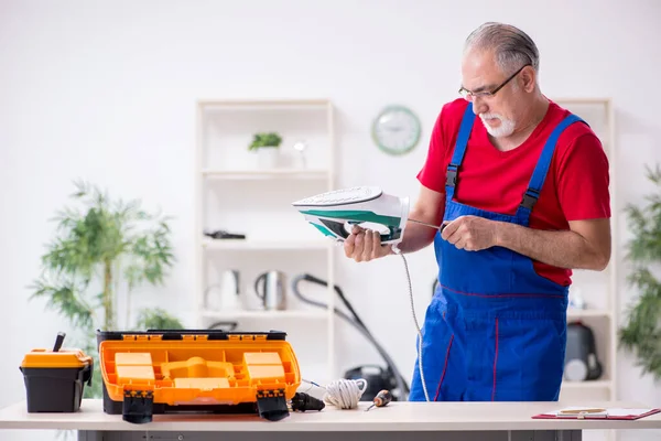 Oude mannelijke aannemer repareert ijzer binnen — Stockfoto