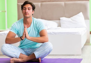 Pijamalı genç adam sabah egzersizi yapıyor.