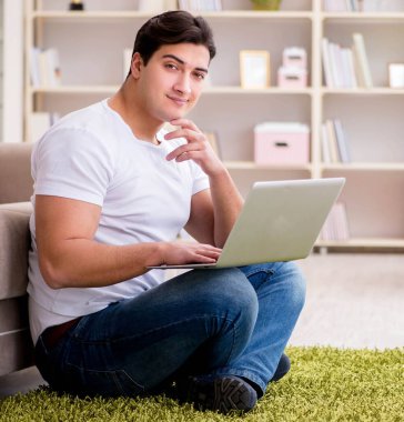 Evde, halı döşemesinde dizüstü bilgisayarda çalışan bir adam.