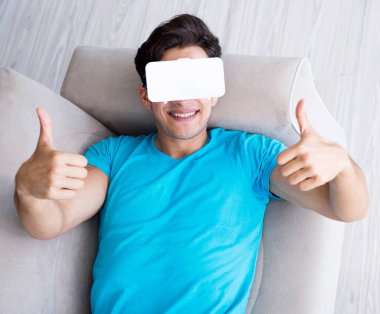 VR gözlüklü genç adam kanepede dinleniyor.