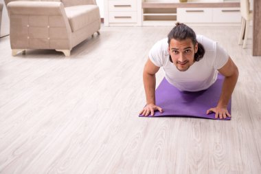 Genç adam evde fiziksel egzersiz yapıyor.