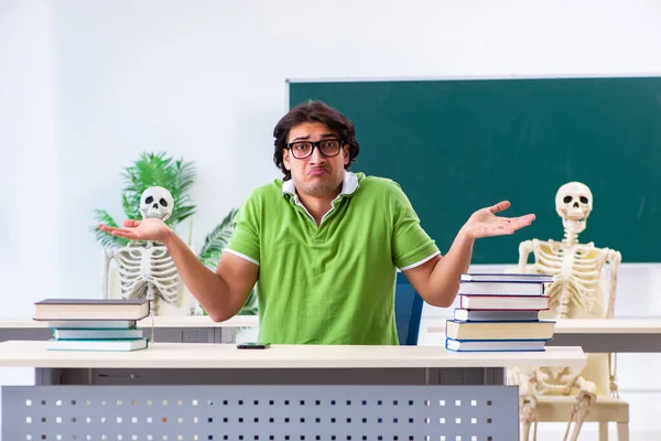 Estudante masculino engraçado na sala de aula com esqueleto — Fotografia de Stock