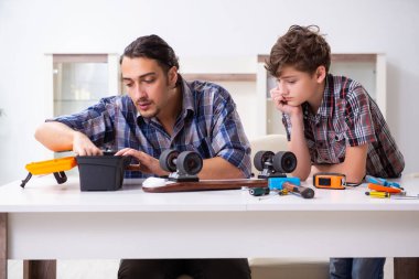 Genç baba oğluyla kaykay tamir ediyor.