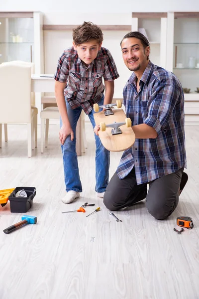 Giovane padre che ripara skateboard con suo figlio a casa — Foto Stock