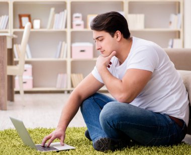 Evde, halı döşemesinde dizüstü bilgisayarda çalışan bir adam.