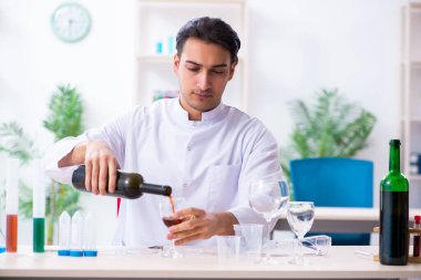 Erkek kimyager laboratuvarda şarap örneklerini inceliyor.