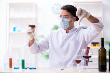 Erkek kimyager laboratuvarda şarap örneklerini inceliyor.