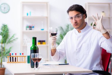 Erkek kimyager laboratuvarda şarap örneklerini inceliyor.