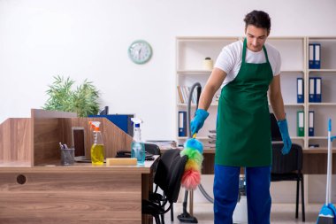 Genç yakışıklı müteahhit ofisi temizliyor.