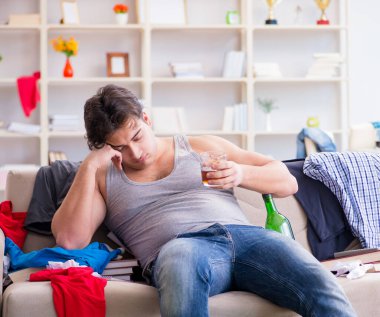 Dağınık bir odada alkol alan genç bir öğrenci.