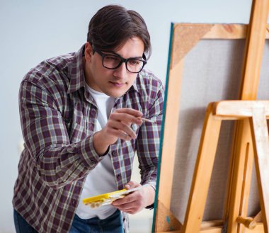 Genç erkek sanatçı parlak stüdyoda resimler çiziyor.