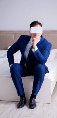 Yatak odasında sanal gerçeklik kulaklığı takan bir iş adamı.