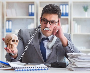 Ofisteki işadamı elinde insan kafatasıyla sigara içiyor.