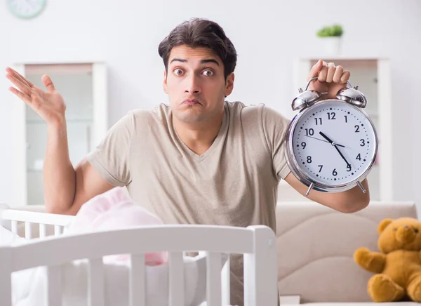 Mladý táta s hodinami v blízkosti novorozenecké postýlky — Stock fotografie