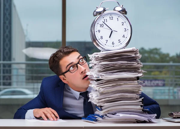 Yığınla evrak işi ve alarm sistemi olan bir iş adamı.