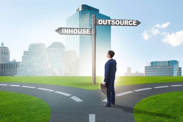 Businessman at crossroads deciding between outsourcing and inhou — Stock Photo, Image