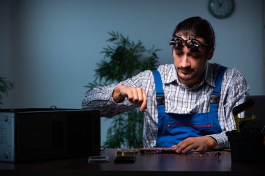 Genç erkek teknisyen geceleri atölyede bilgisayar tamir ediyor.