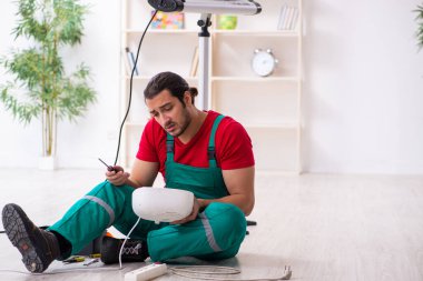 Genç erkek müteahhit içeride fan ısıtıcıyı tamir ediyor.