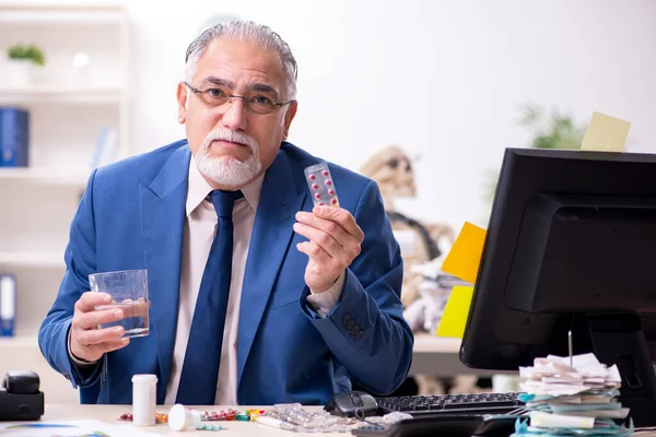 Old male sick employee working overtime in the office