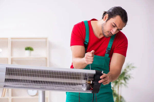 Young male contractor repairing heater indoors