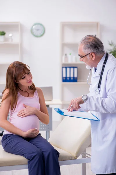 Молодая беременная женщина посещает пожилого врача-гинеколога — стоковое фото