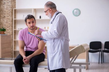 Genç erkek hasta yaşlı erkek doktoru ziyaret ediyor.