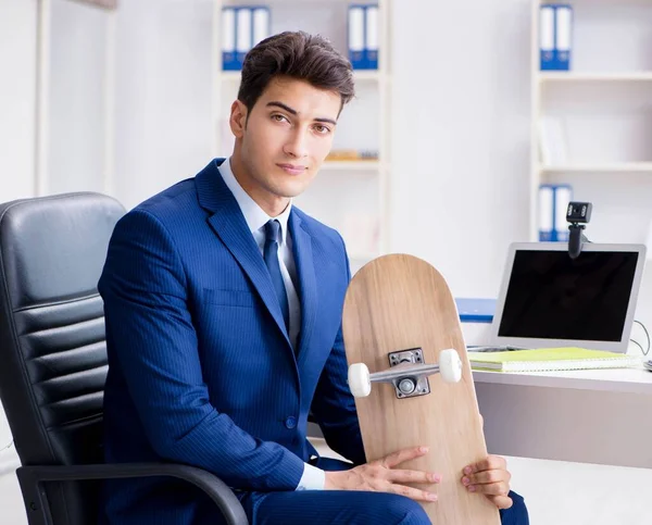 Jovem empresário com skate no escritório em conceito de esportes — Fotografia de Stock