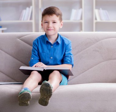 Evde kitap okuyan küçük bir çocuk.