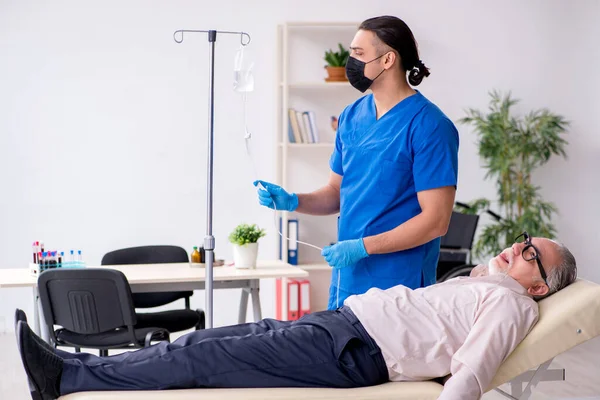 Old patient visiting young male doctor for intravenous therapy — Stock Photo, Image