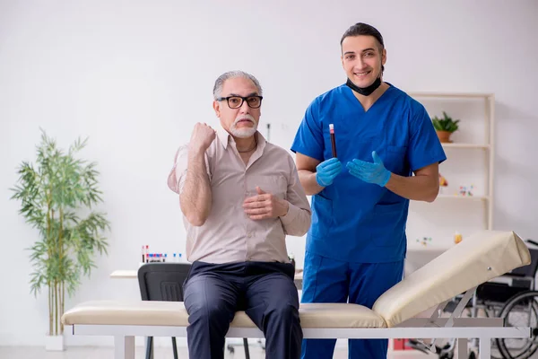 Paciente anciano que visita al joven médico en el concepto de muestreo de sangre — Foto de Stock
