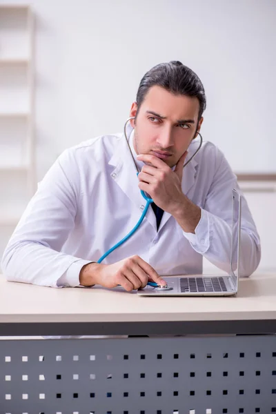 Joven doctor masculino con estetoscopio reparando computadora —  Fotos de Stock