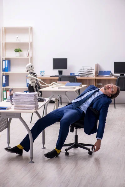Jovem funcionário do sexo masculino com esqueletos no escritório — Fotografia de Stock